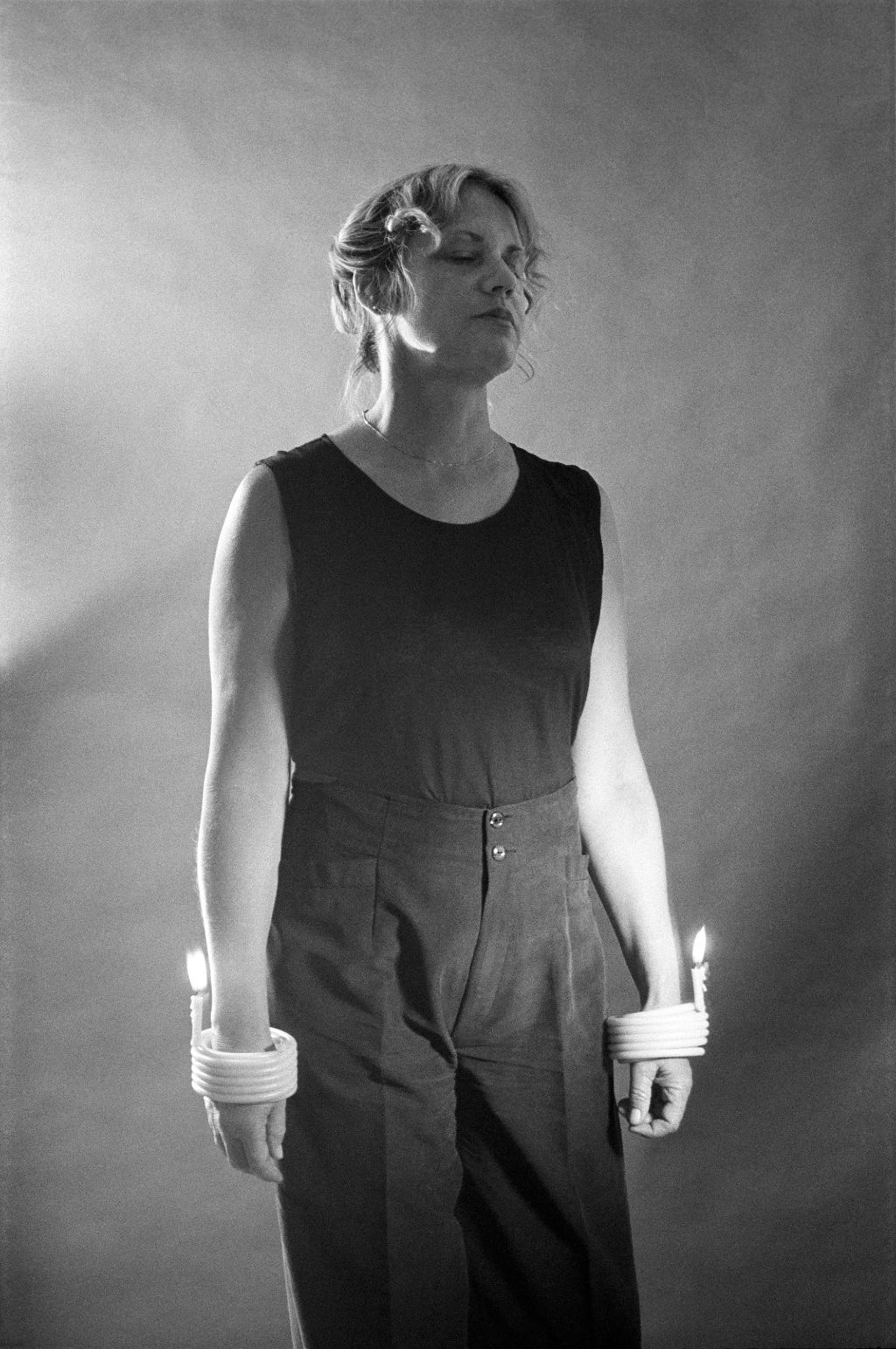 A woman in black with closed eyes, her wrists encircled by burning candles