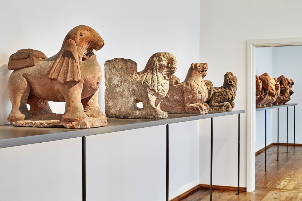 Löwenskulpturen aus Stein stehen auf einem Metalltisch in einem hellen Museumsraum