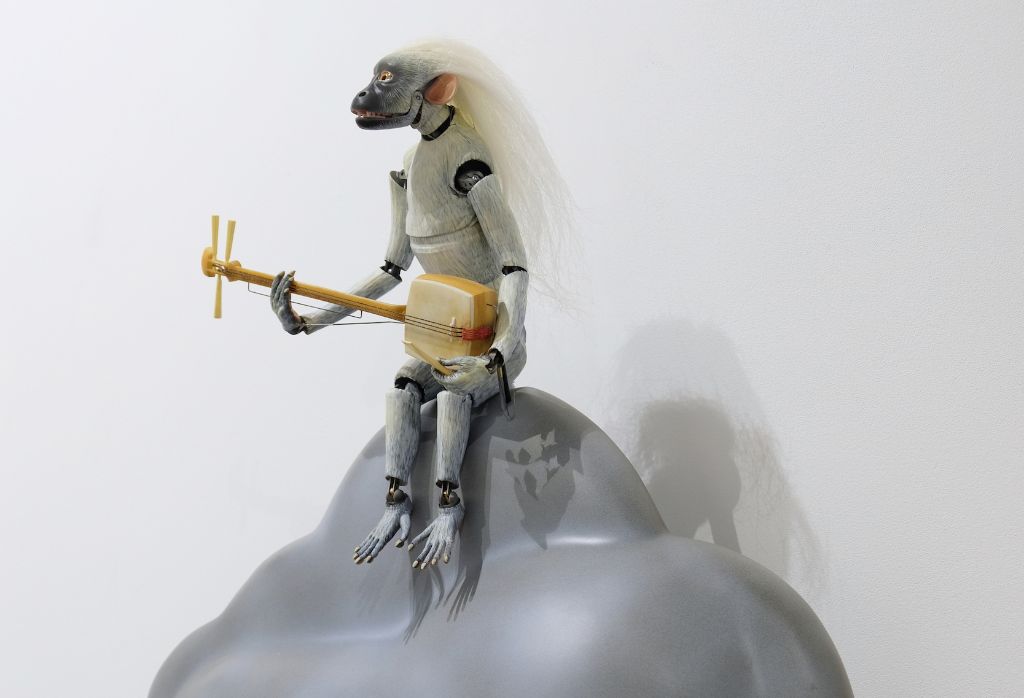 Eine skurrile Affenfigur mit langen weissen Haaren spielt ein Banjo, sitzt auf einer grauen Wolke