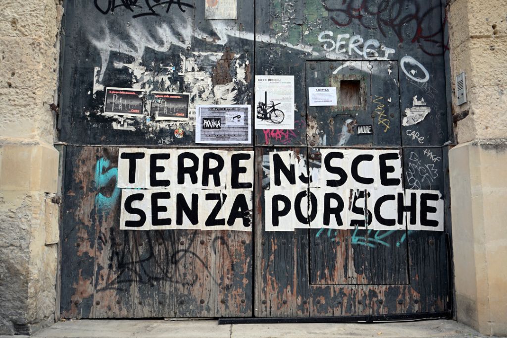 Ein altes, mit Graffiti bedecktes Tor zeigt Plakate und den Schriftzug „Terre Nsce Senza Porsche“.