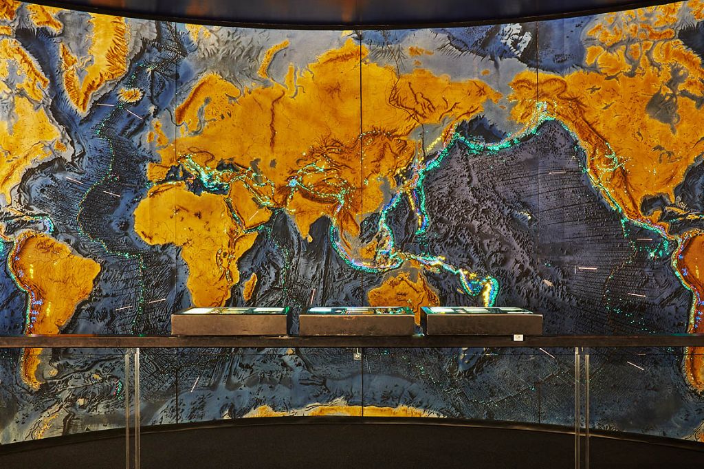 Eine grosse Weltkarte zeigt Erdplatten und Vulkangürtel in leuchtenden Farben.